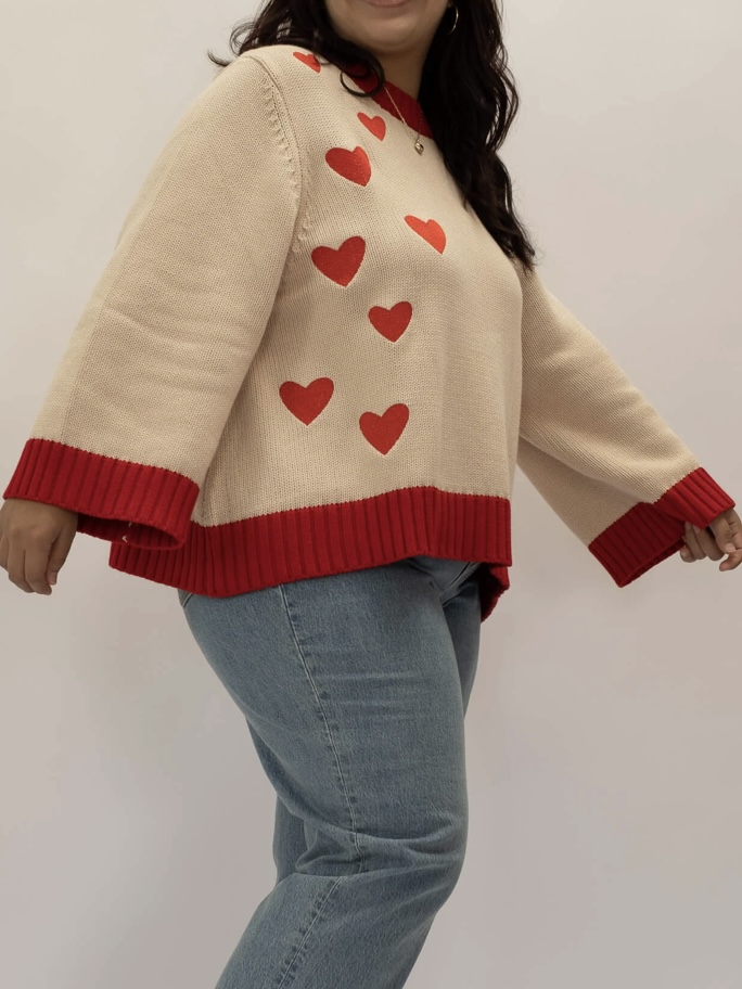 A broken white and red plus-sized sweater with red hearts adorning its right side.