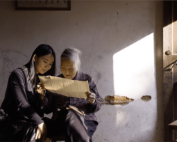 Hu Xin, a young Chinese woman, sits next to He Yan Xin, an older Chinese woman as they both read a paper scroll. Picture is taken from the documentary Hidden Letters.