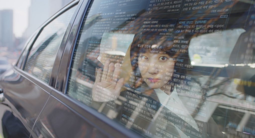 Extraordinary Attorney Woo: Woo Young-woo is looking out from a car window, scanning the imaginative wall of text in Korean on the window as she is analyzing its content.