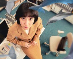 Woo Young-woo, the protagonist of Extraordinary Attorney Woo, looking upwards. She has short black hair with bangs and wears a camel brown suit and skirt. She is surrounded by floating dolphins and whales.