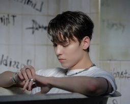 Vernon of SEVENTEEN sitting in a bathtub, surrounded by walls filled with graffiti here and there. His look is emo.