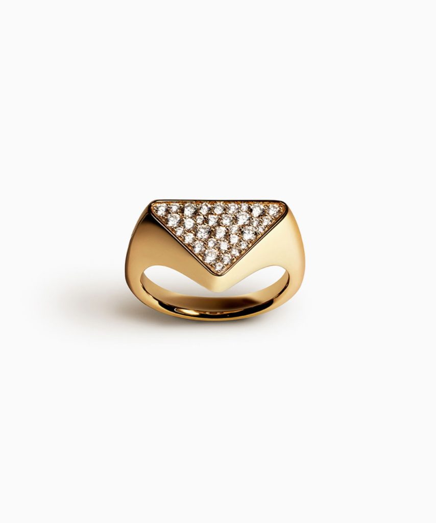 A golden ring with several gems sitting on top of it inside a triangular hole from Prada's Eternal Gold collection.
