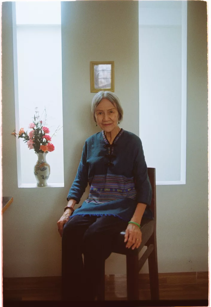 Trần Thị Tuyết Hoa, Tram Anh Nguyen's paternal grandmother, sitting on a wooden chair next to a windowsill.