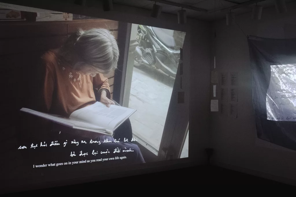 A projected screen in "Hoa", an exhibition by Tram Anh Nguyen, which shows his grandmother reading a book.