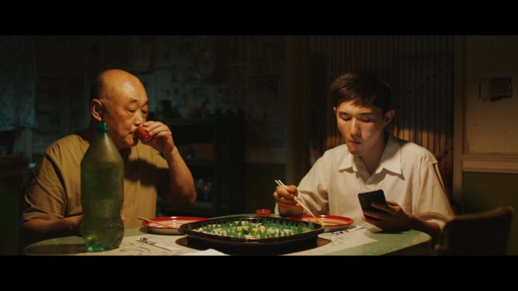An elderly father and his adult son sitting on the dining table; still from Plum Town (2020). Courtesy of Kelly Yu.