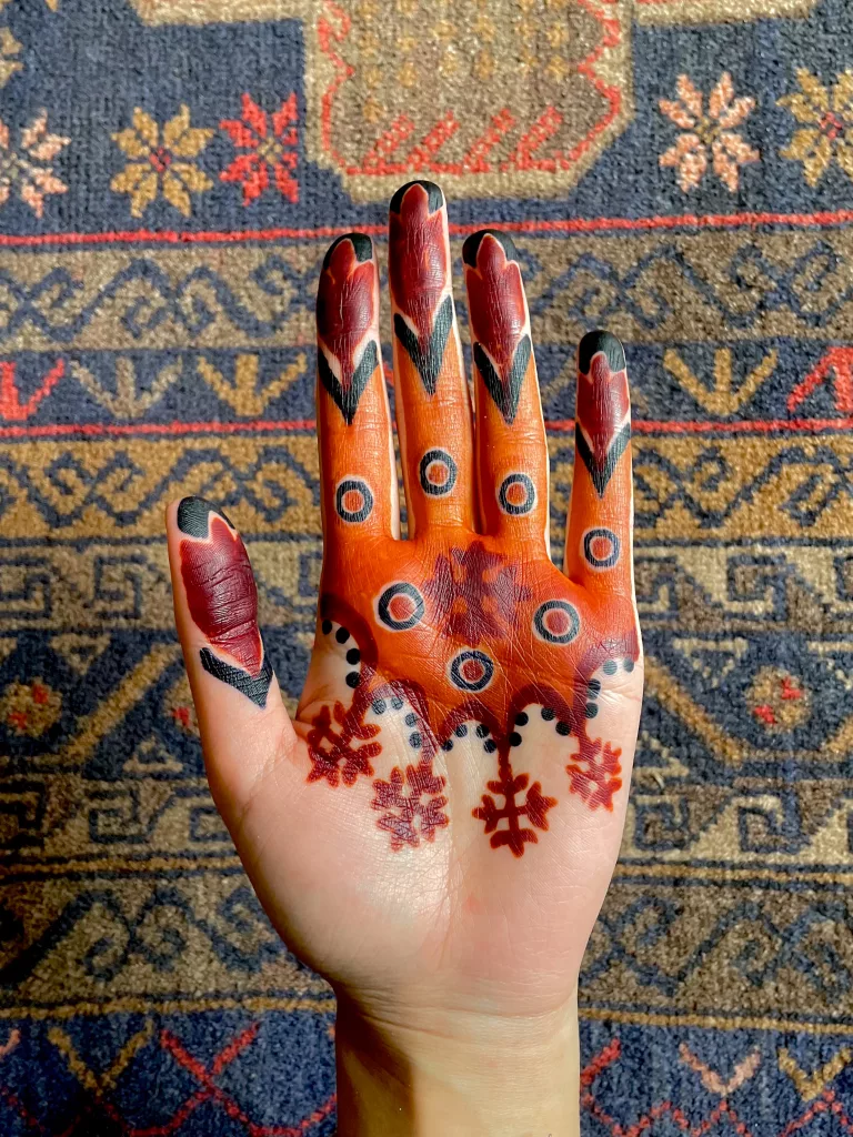 A red, black, and orange henna art on a palm.