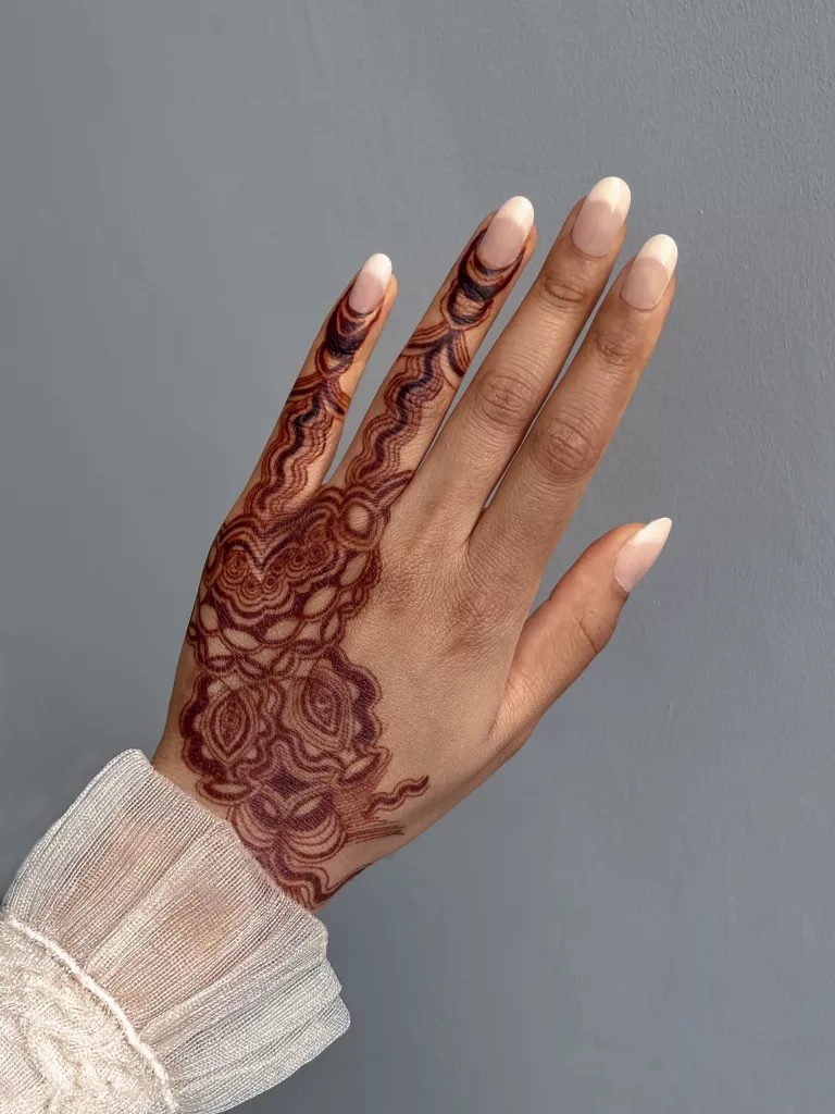Maroon floral pattern painted on the back of a hand, which branches to the pinky and ring fingers