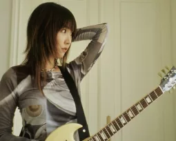MEMI looking sideways, her guitar strapped to her body.