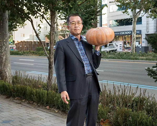 An elderly Korean man holding a pumpkin on his left hand.