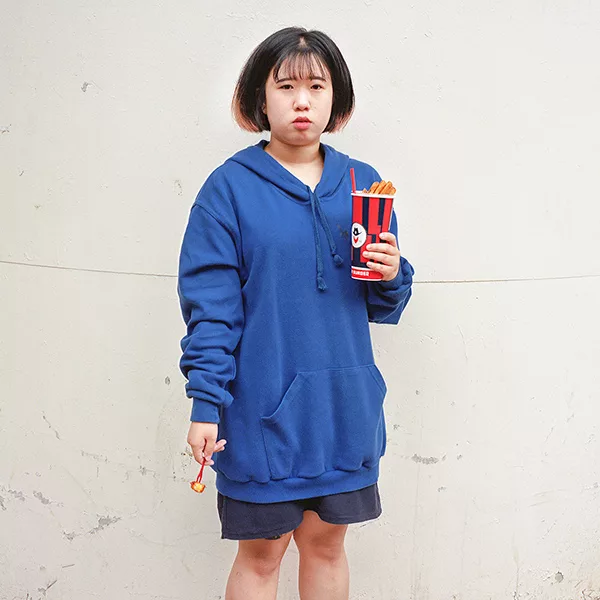 Haneul Lee - A woman with short hair, gray shorts, and dark blue hoodie. She is holding a cup of snacks.
